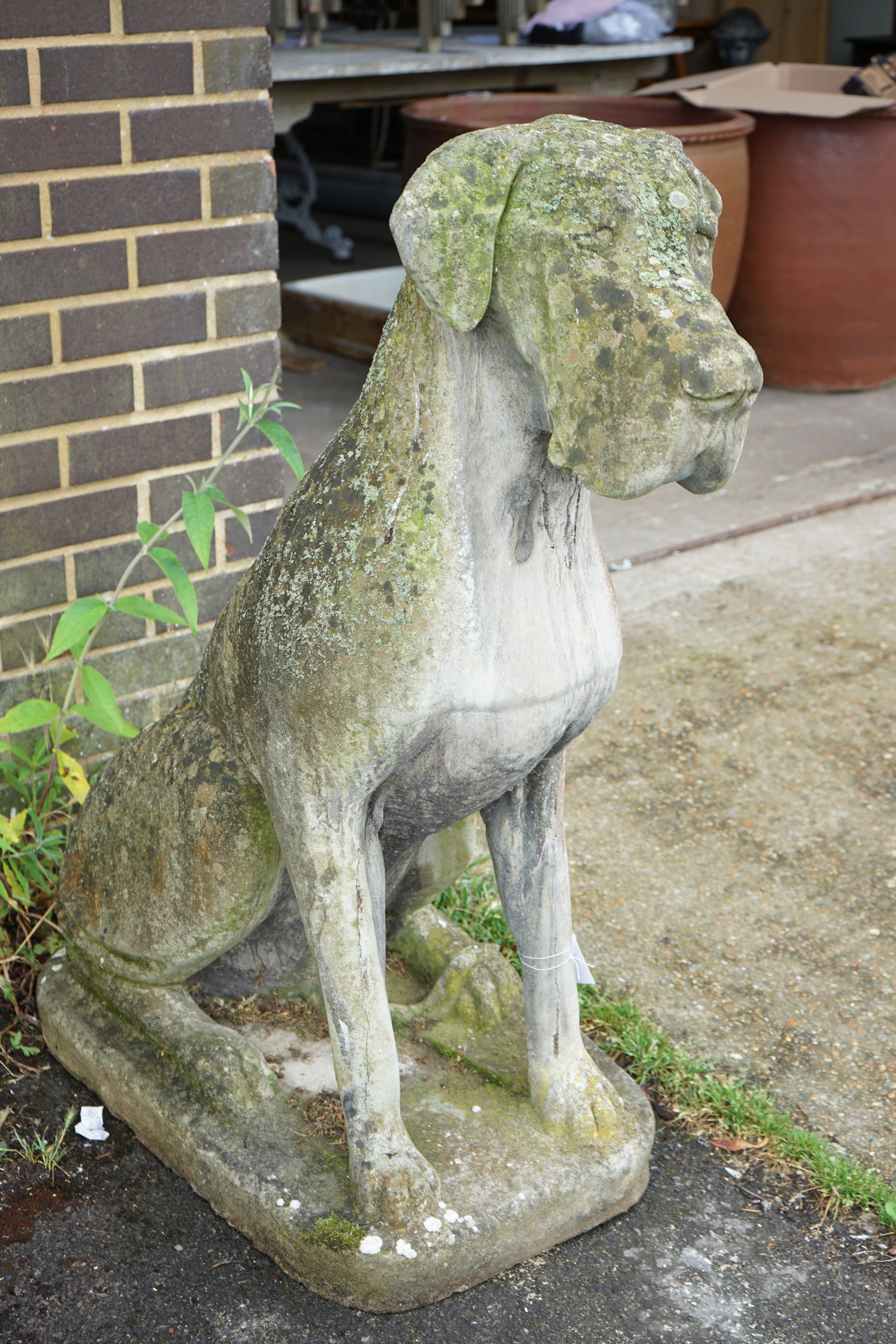 A large weathered reconstituted stone garden ornament modeled as a seated Great Dane, height 116cm